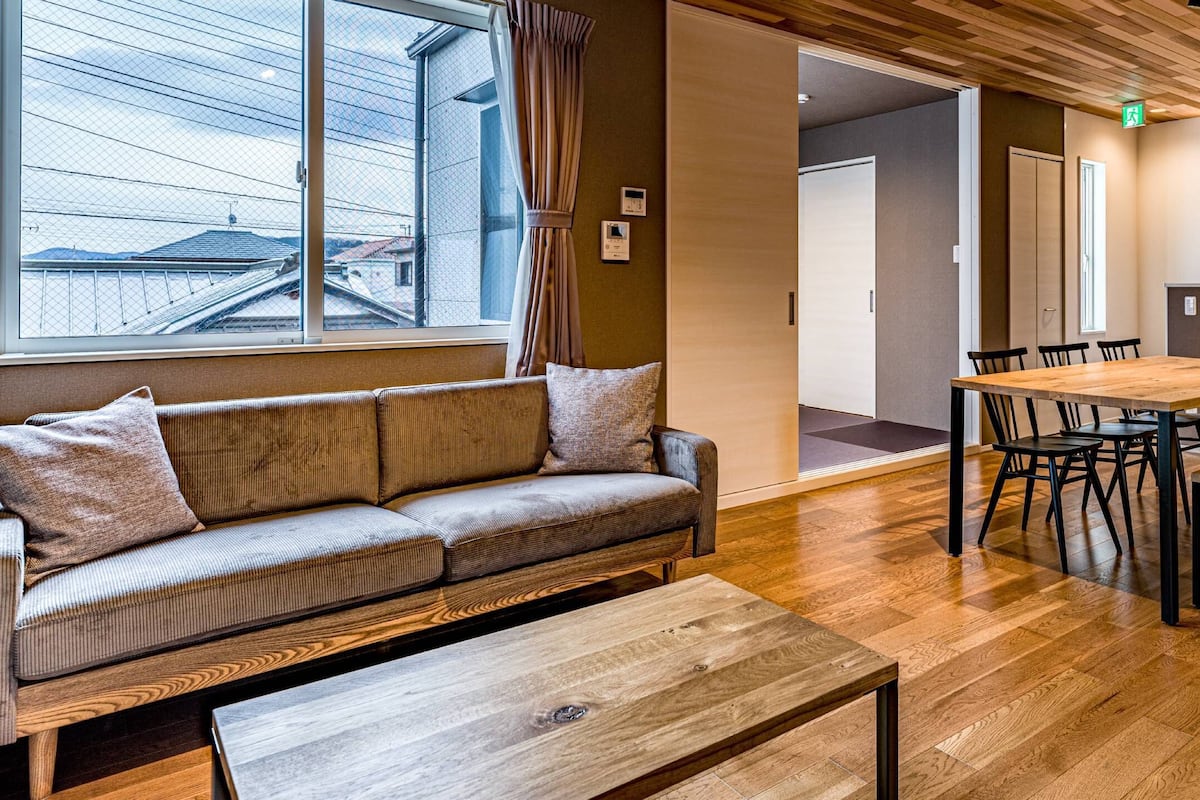 A modern interior with a wooden floor, a sofa with cushions, a dining table with chairs, and a bench.