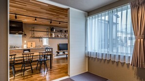 A modern kitchen with wooden cabinetry, a dining area with a wooden table and chairs, and a large window with sheer curtains. - Rakuten STAY HOUSE x WILL STYLE Fujinomiya (Fujinomiya)