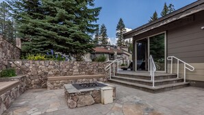 A stone patio with a fire pit, a stone wall, and a building with a covered entrance. - Chamonix #62 Bldg. D (Mammoth Lakes)