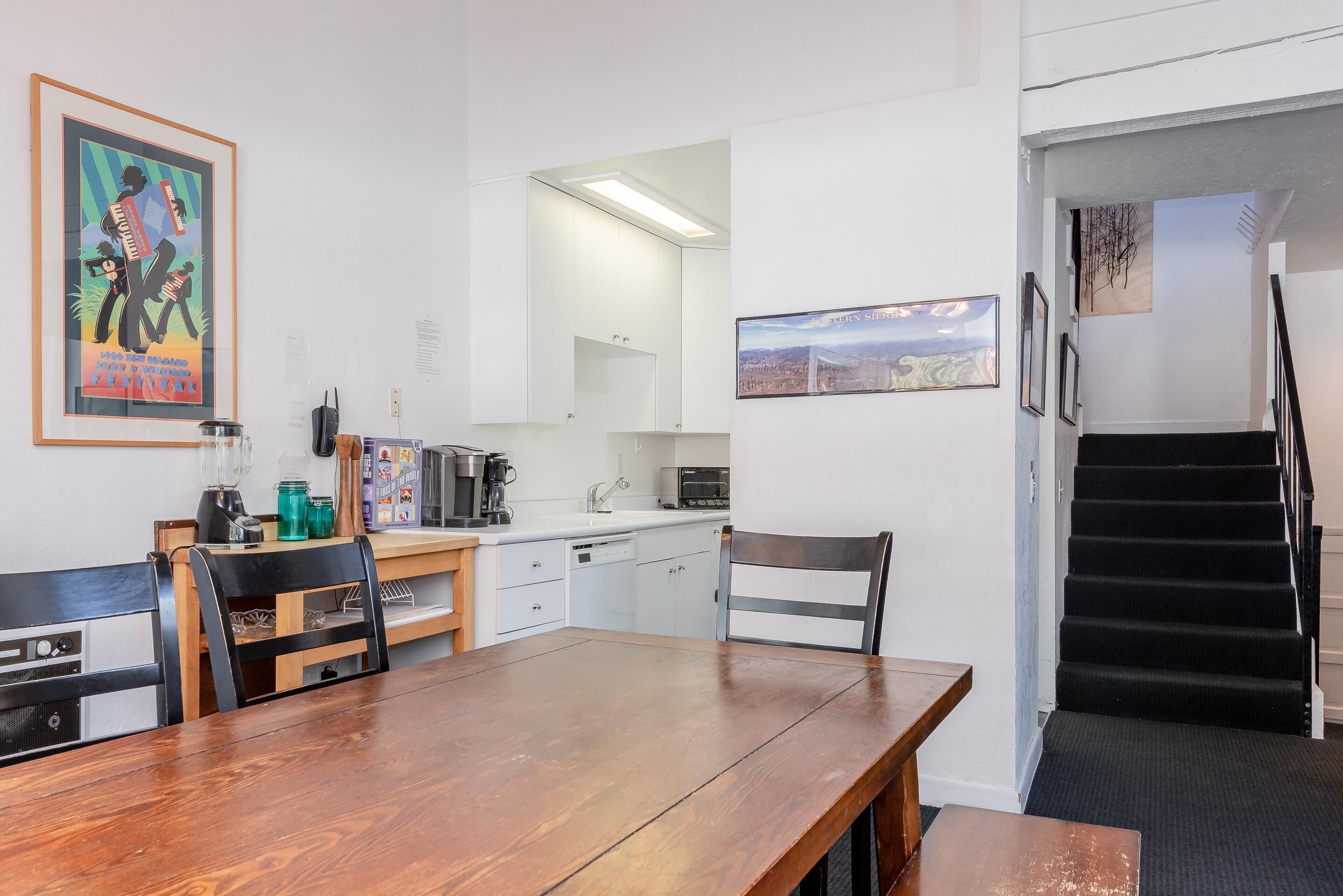 A modern kitchen with white cabinets, a wooden dining table, and a staircase leading to an upper floor.