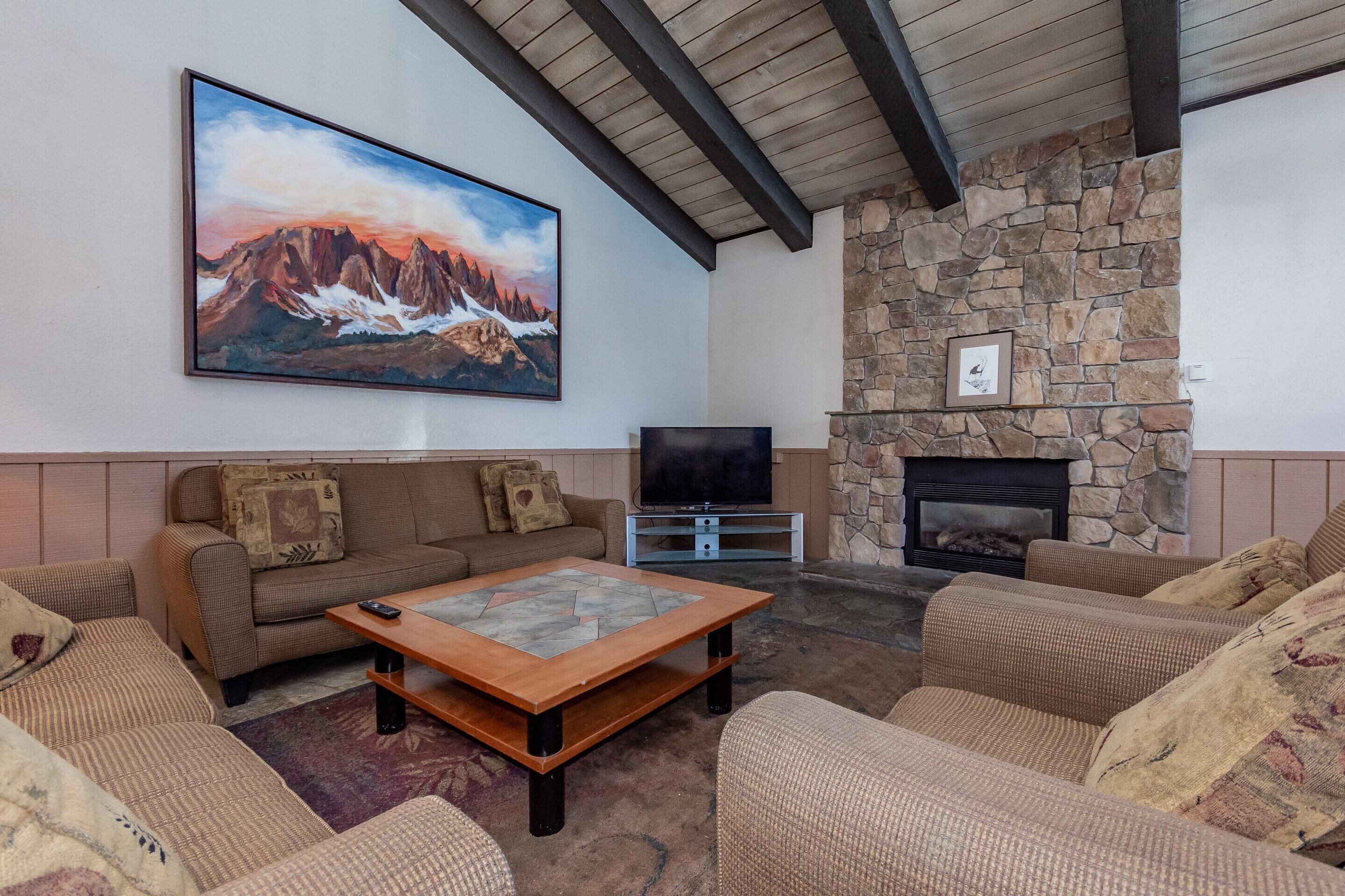 A cozy living room with a stone fireplace, a large painting of mountains, and comfortable seating.