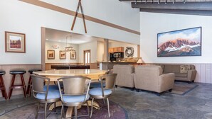 A dining area with a round table and chairs, a kitchen in the background, and a large painting on the wall. - Chamonix #62 Bldg. D (Mammoth Lakes)