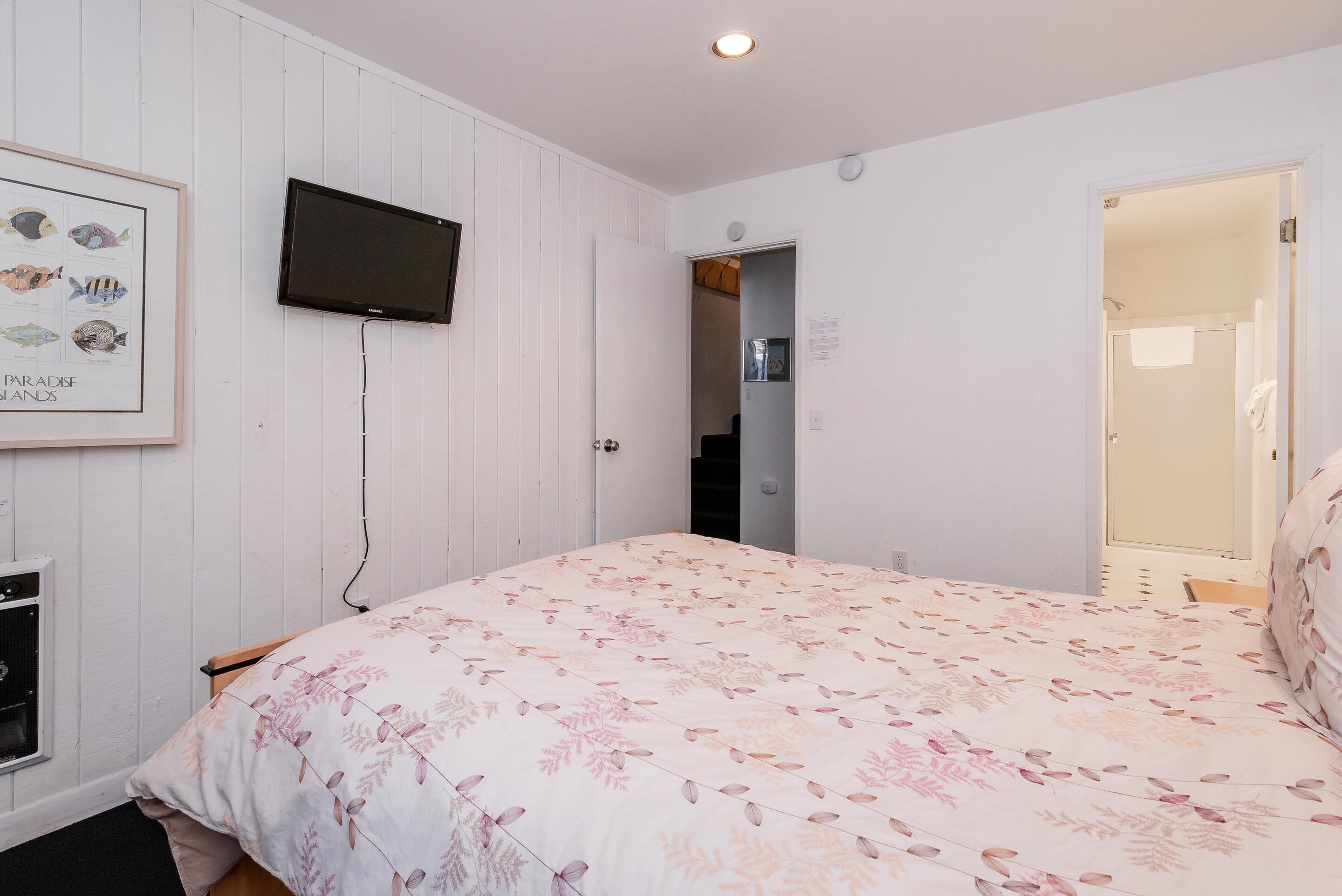A bedroom with a bed, a television mounted on the wall, and a door leading to another room.
