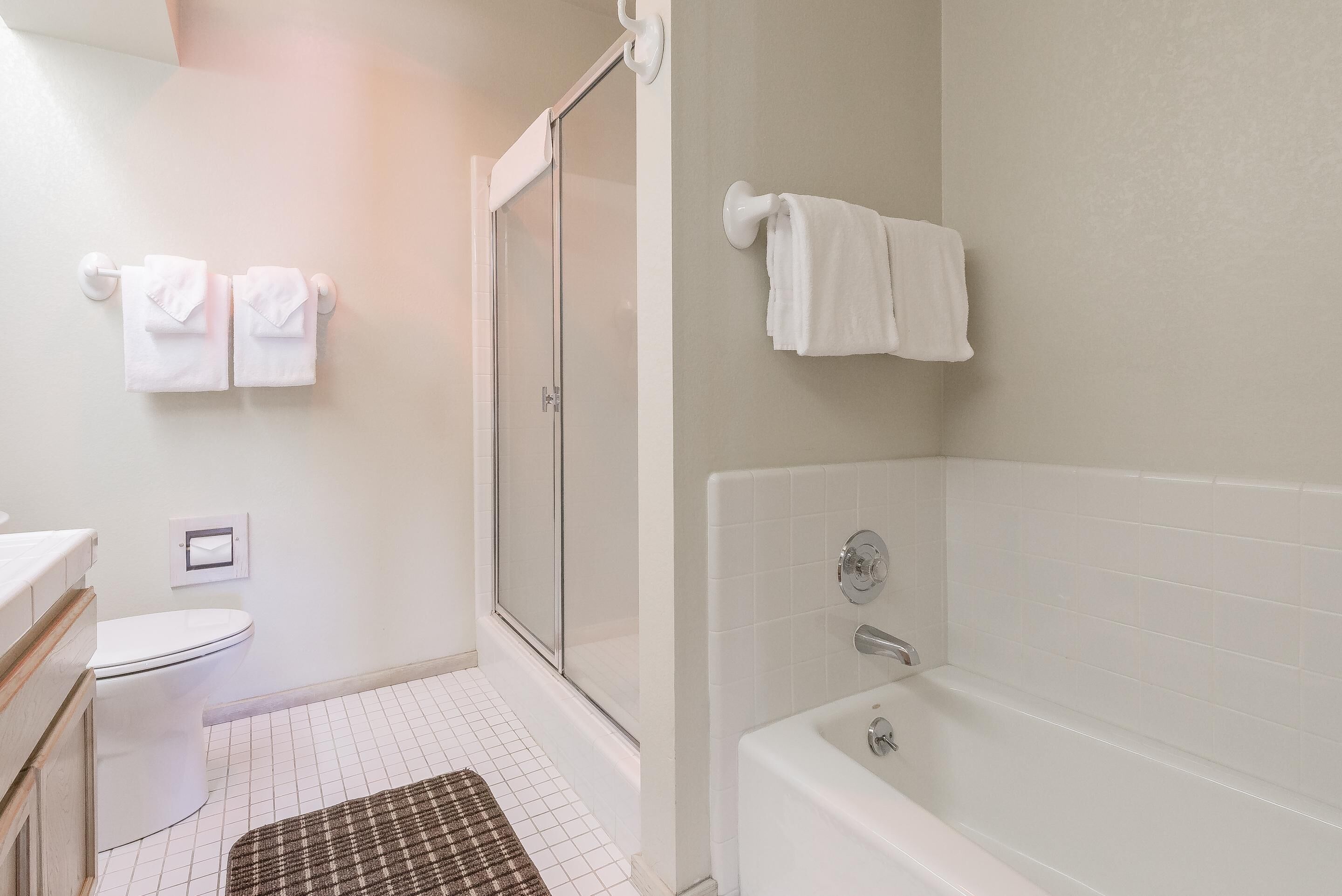 A bathroom with a toilet, shower, and bathtub. There are towels hanging on a rack and a rug on the floor.