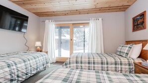 Una habitación con dos camas, un televisor montado en la pared, una ventana con cortinas y un cuadro en la pared.