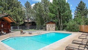 Una piscina rectangular con borde de azulejos, rodeada por una terraza de madera. Se observan sillas de descanso y una pequeña estructura de madera cerca.
