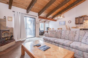 A cozy living room with a fireplace, a sofa, a coffee table, and a kitchen area. - Chateau Blanc #13 (Mammoth Lakes)