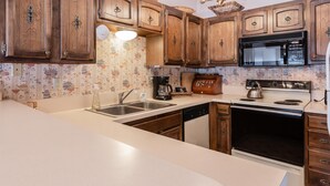 Una cocina con armarios de madera, microondas, estufa, fregadero y una lámpara de araña.