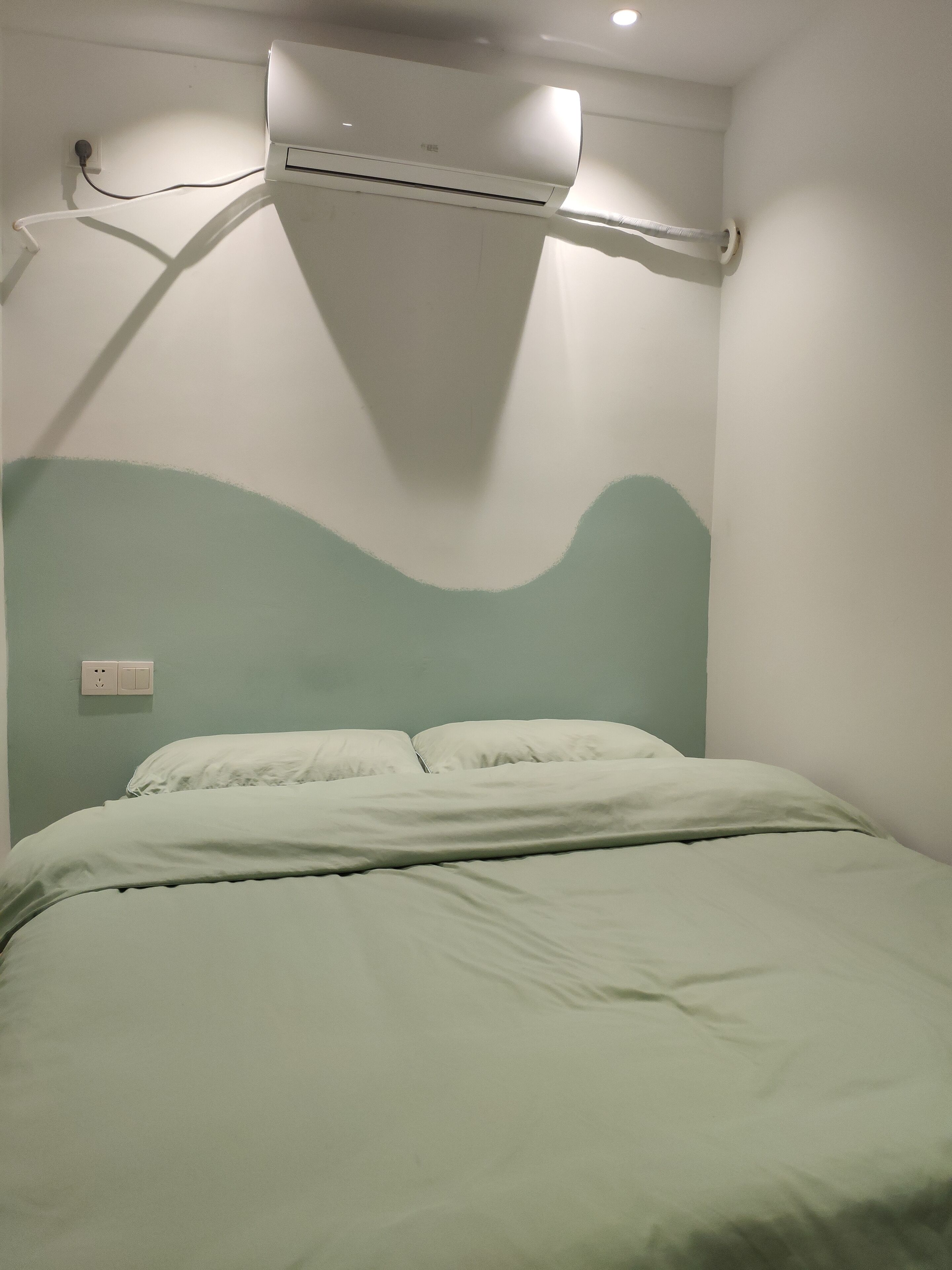 A room with a bed, a wall-mounted air conditioner, and a power outlet.