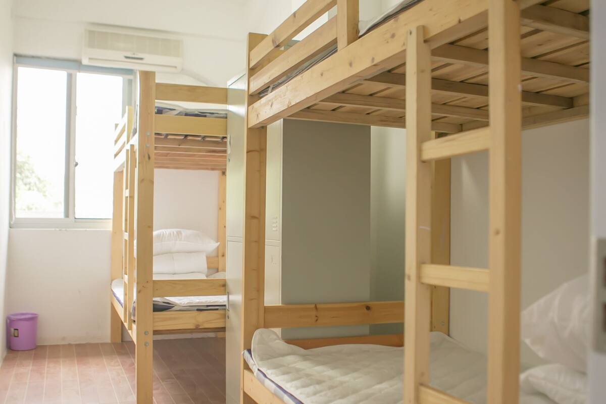 A dormitory room with bunk beds, a window, and a wooden floor.