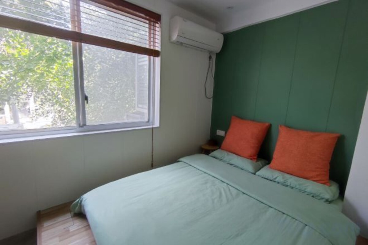 A bedroom with a bed, a window with blinds, and a green wall.