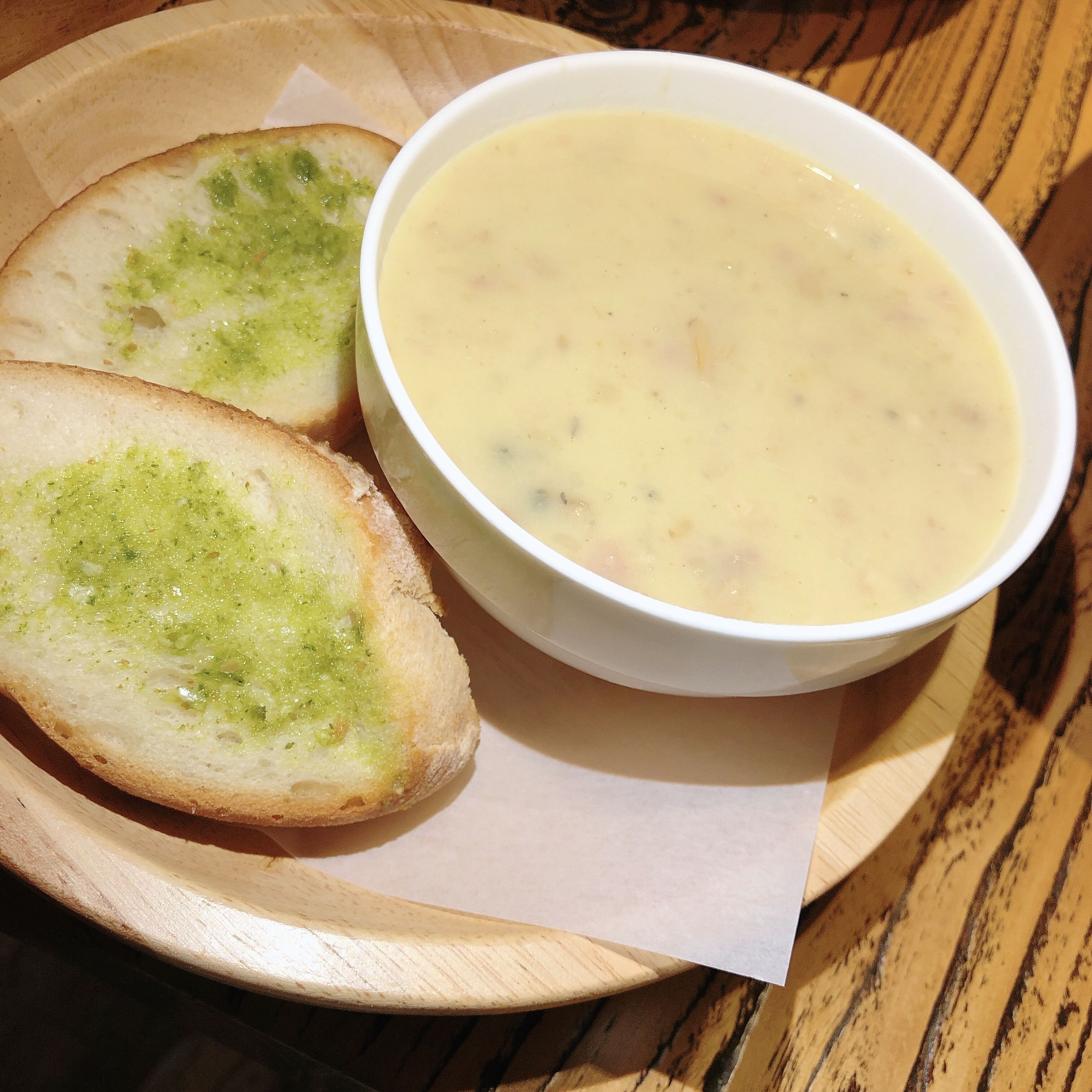 Una ciotola di zuppa dalla consistenza cremosa e due fette di pane con crema verde su un vassoio di legno.