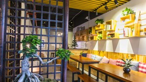 A cozy restaurant with wooden tables and benches, a bamboo partition, and shelves with books and plants. - Suzhou Blue Gate Hostel (Suzhou)
