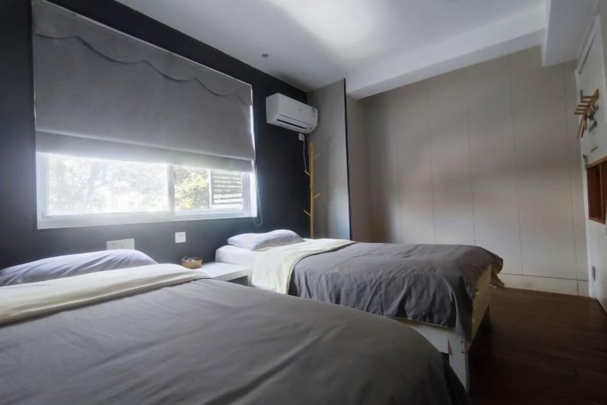A hotel room with two beds, a window with curtains, an air conditioning unit, and a wooden floor.