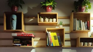 A cozy living room with wooden shelves holding books, a board game, and potted plants. - Suzhou Blue Gate Hostel (Suzhou)