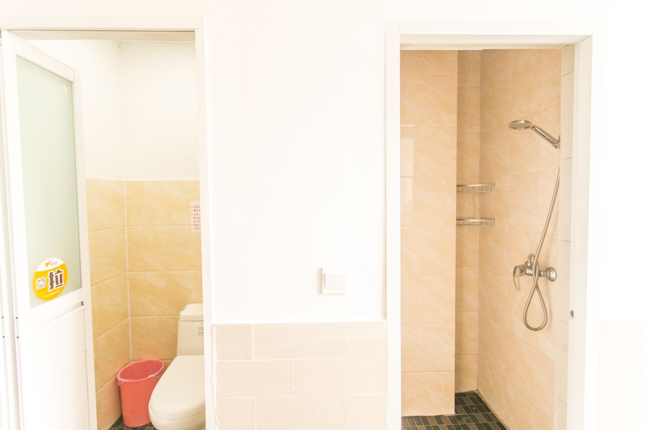 A bathroom with a toilet, a shower, and a trash bin.