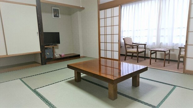 A traditional Japanese room with tatami flooring, a low wooden table, a TV on a shelf, and a sliding shoji screen. - Hotel New Otsuka (Shirako)