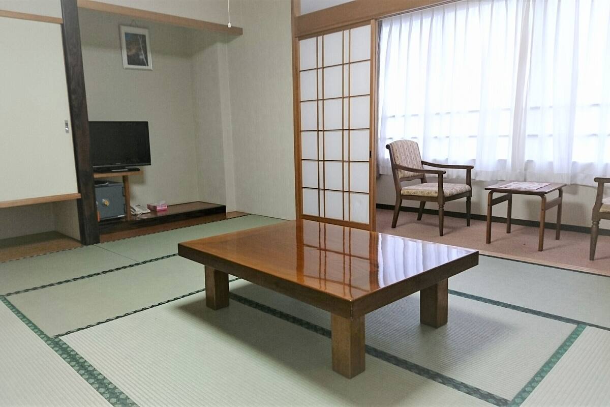 A traditional Japanese room with tatami flooring, a low wooden table, a TV on a shelf, and a sliding shoji screen.