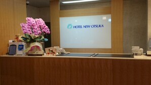 A reception desk with a floral arrangement, a digital screen displaying "HOTEL NEW OTSUKA", and various reception items. - Hotel New Otsuka (Shirako)