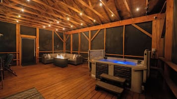 An indoor wooden deck with a hot tub, seating area, and a fireplace.