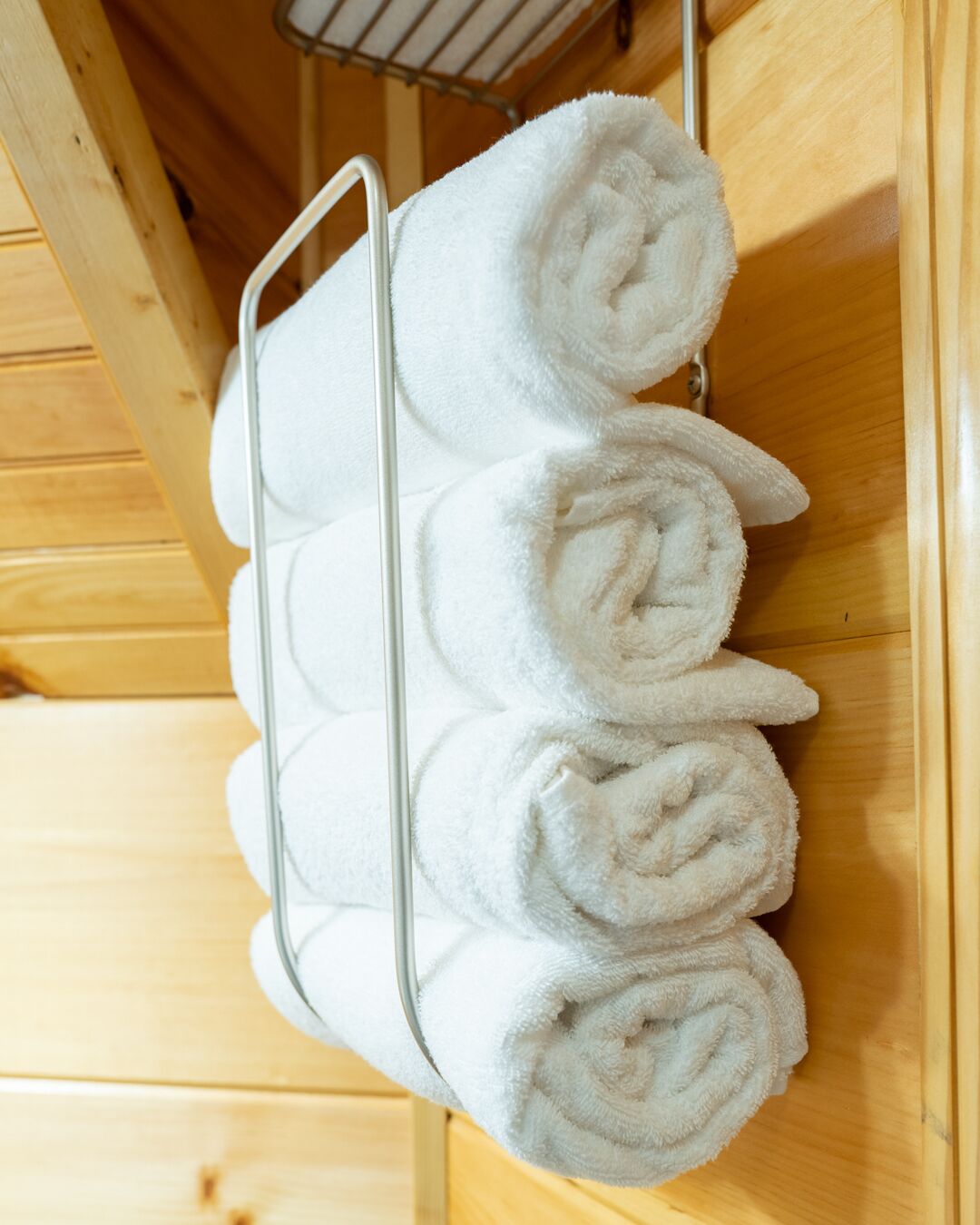 Un porte-serviettes en métal, avec quatre serviettes blanches soigneusement pliées, adossé à un mur en bois.