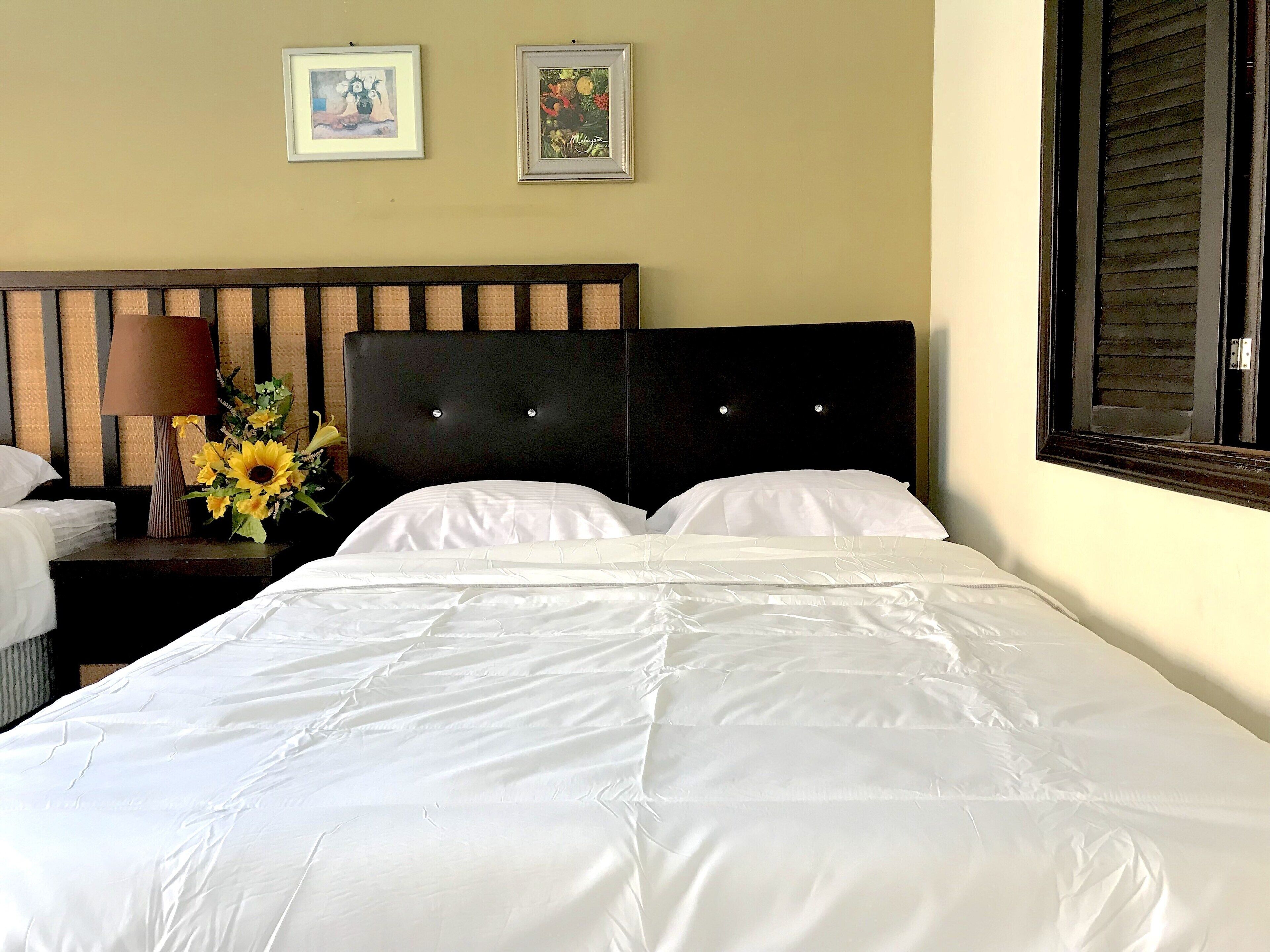 A neatly made bed with white linens, a dark headboard, and a nightstand with a lamp and a vase of sunflowers.