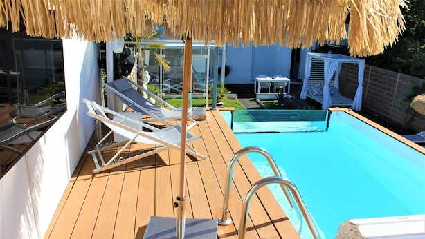 A wooden deck with a pool, lounge chairs, and a thatched umbrella. - The White Home Broadway, Luxury Jacuzzi, exclusive private heated pool  (Châteauroux)