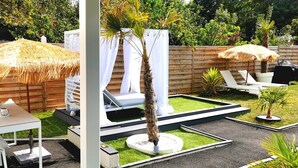 A patio with a table and chairs, a thatched umbrella, a white chair, and a small palm tree. - The White Home Broadway, Luxury Jacuzzi, exclusive private heated pool  (Châteauroux)
