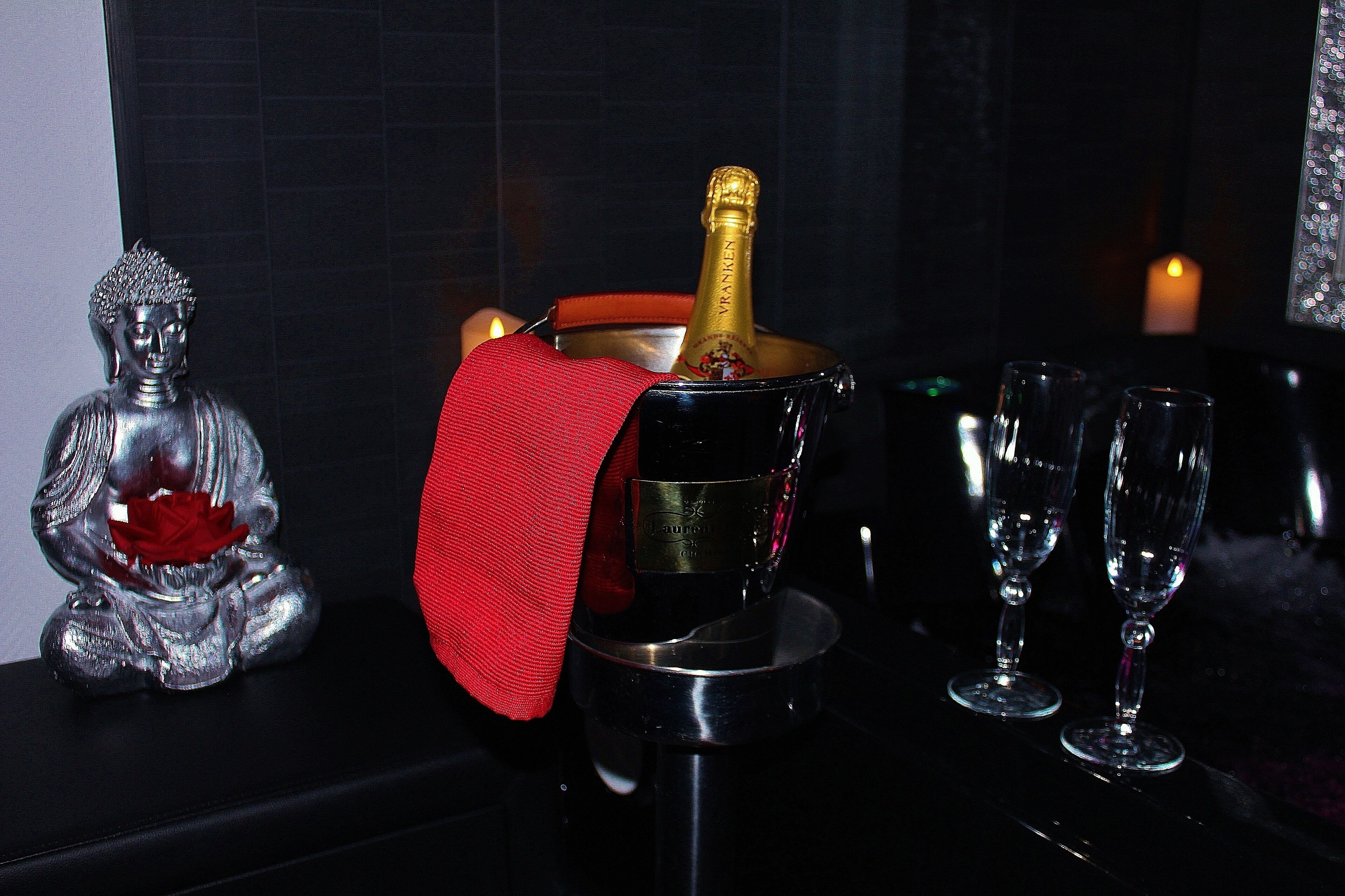 Een tafel met een champagnefles, twee glazen en een Boeddhabeeld.