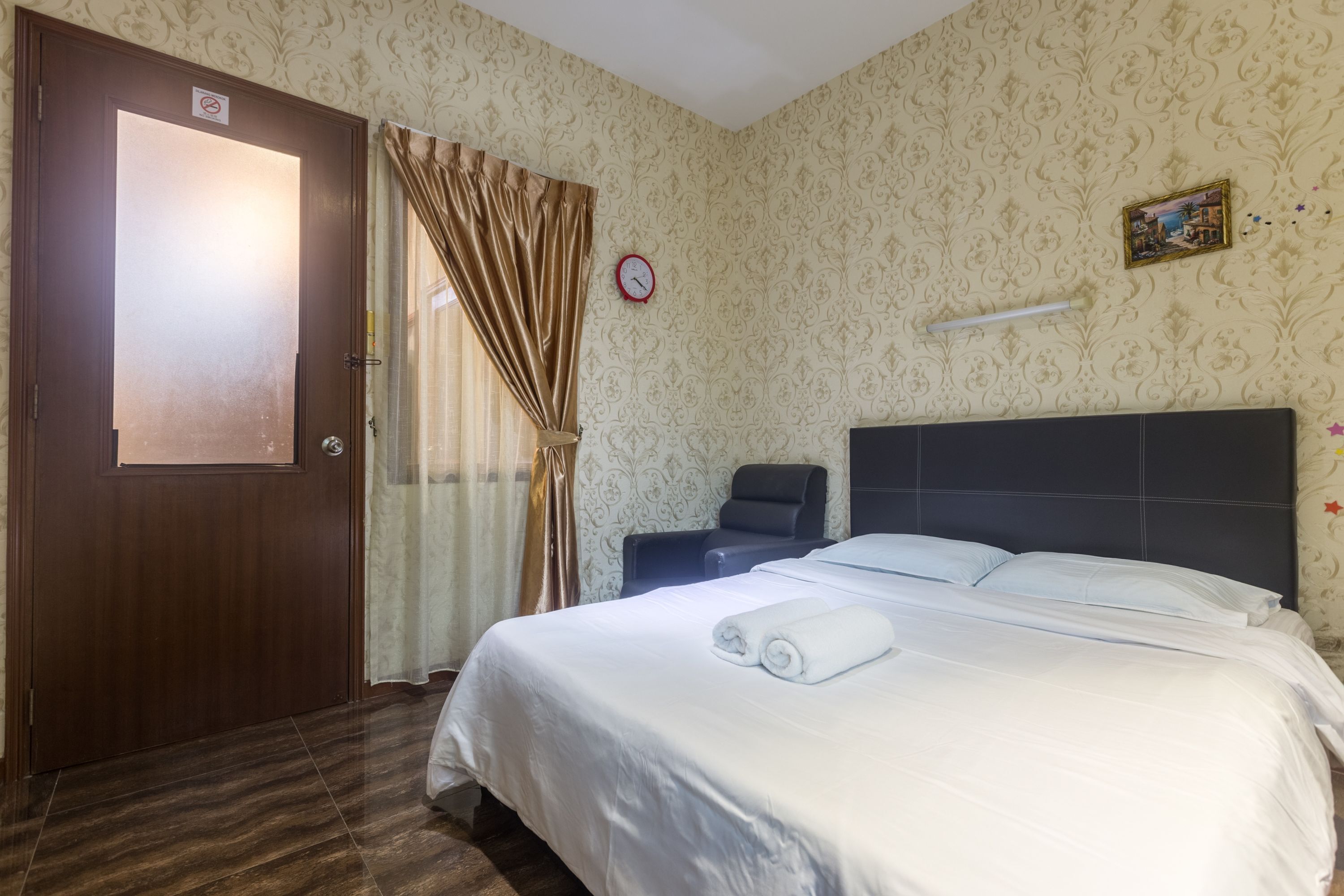 A hotel room with a bed, a chair, a door, and a clock on the wall.