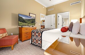 A hotel room with a bed, a TV, a wardrobe, and a chair. - Maui Resort Rentals:  Honua Kai Hokulani 111 – Ground Floor Interior Courtyard 2BR, Steps to Pools, Beach, and BBQs, Large Lawn Area! (Lahaina)
