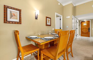 A dining area with a wooden table set for four, surrounded by wicker chairs. - Maui Resort Rentals:  Honua Kai Hokulani 111 – Ground Floor Interior Courtyard 2BR, Steps to Pools, Beach, and BBQs, Large Lawn Area! (Lahaina)