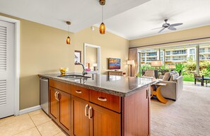 A modern kitchen with a granite countertop, wooden cabinets, and a built-in dishwasher. - Maui Resort Rentals:  Honua Kai Hokulani 111 – Ground Floor Interior Courtyard 2BR, Steps to Pools, Beach, and BBQs, Large Lawn Area! (Lahaina)