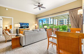 Habitación de hotel con sofá, sillas, televisión y vistas a un edificio y zonas verdes.