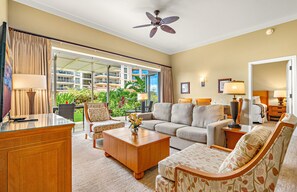 A hotel room with a sofa, chairs, a coffee table, a desk, and a ceiling fan.