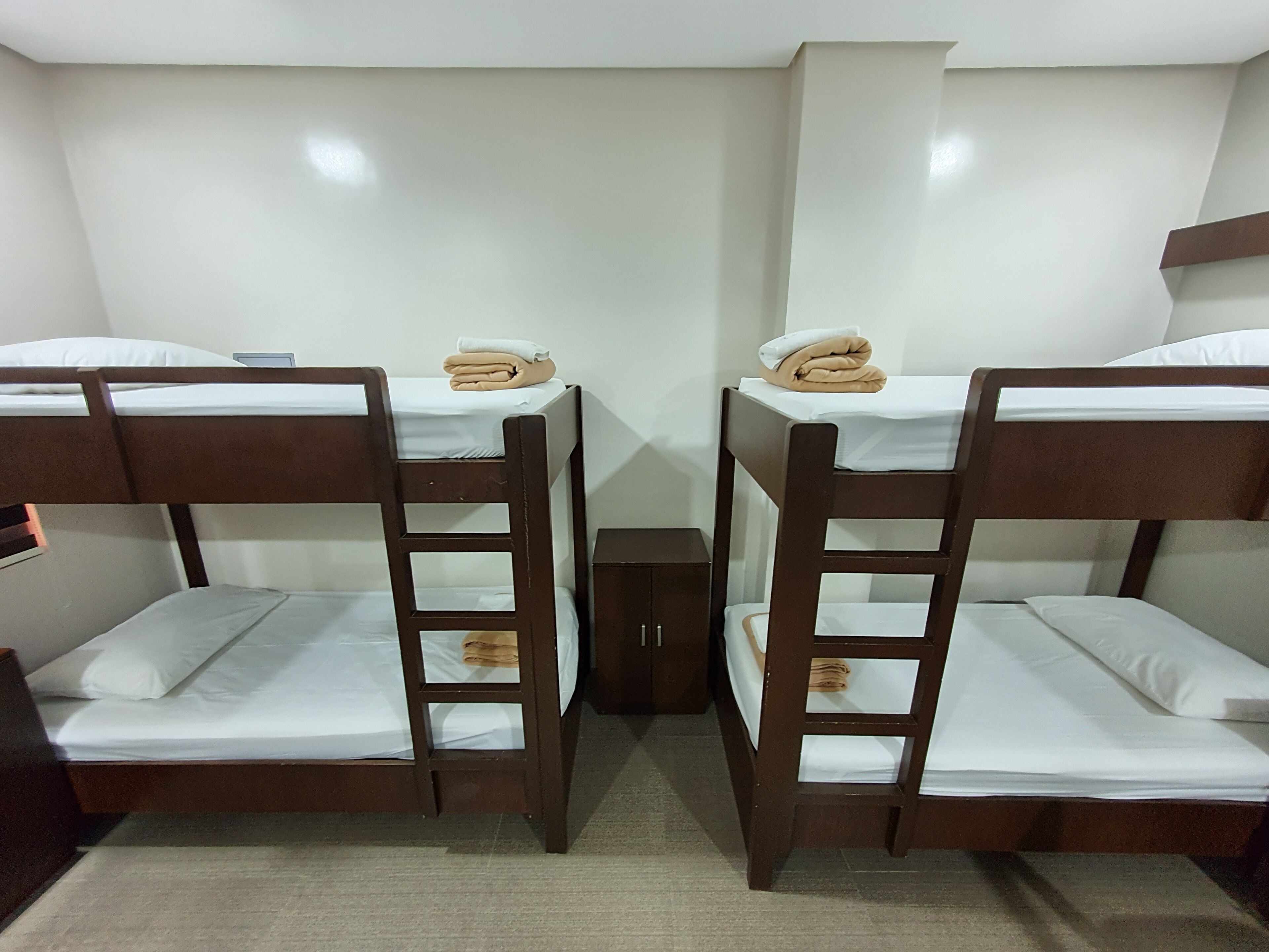 A room with two bunk beds, each with a mattress and a pillow. There is a small cabinet between the beds.