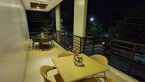 A balcony with a table and chairs, a potted plant, and a view of the street at night. - Missio Dei Hotel (Dipolog)