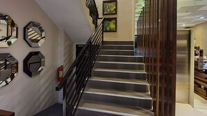 A staircase with a black railing, leading to a landing with a fire extinguisher and a wall with three framed artworks. - Missio Dei Hotel (Dipolog)