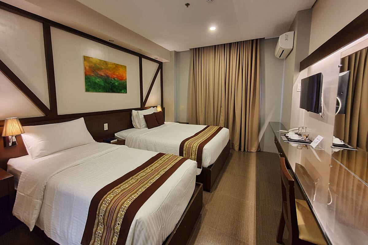 A hotel room with two beds, a desk, a mirror, and a painting on the wall.