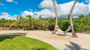 A sandy beach with a hammock, palm trees, and a volleyball net. - 🏖️Private Kona Home w/ Pool, Sand Court & Ocean View Lanai | Nakukui Ekolu (Kailua Kona)