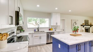 A modern kitchen with white cabinets, a built-in oven, a dishwasher, and a large island with a marble countertop. - Near Golfing & Shops: Scottsdale Gem w/ Patio! (Scottsdale)