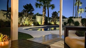 A pool area with a curved edge, surrounded by palm trees and potted plants, with a bench and a table in the foreground. - Near Golfing & Shops: Scottsdale Gem w/ Patio! (Scottsdale)