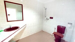 A bathroom with a white tiled wall, a red sink, a mirror, a shower, and a toilet. - Penuin Hotel (Batam)