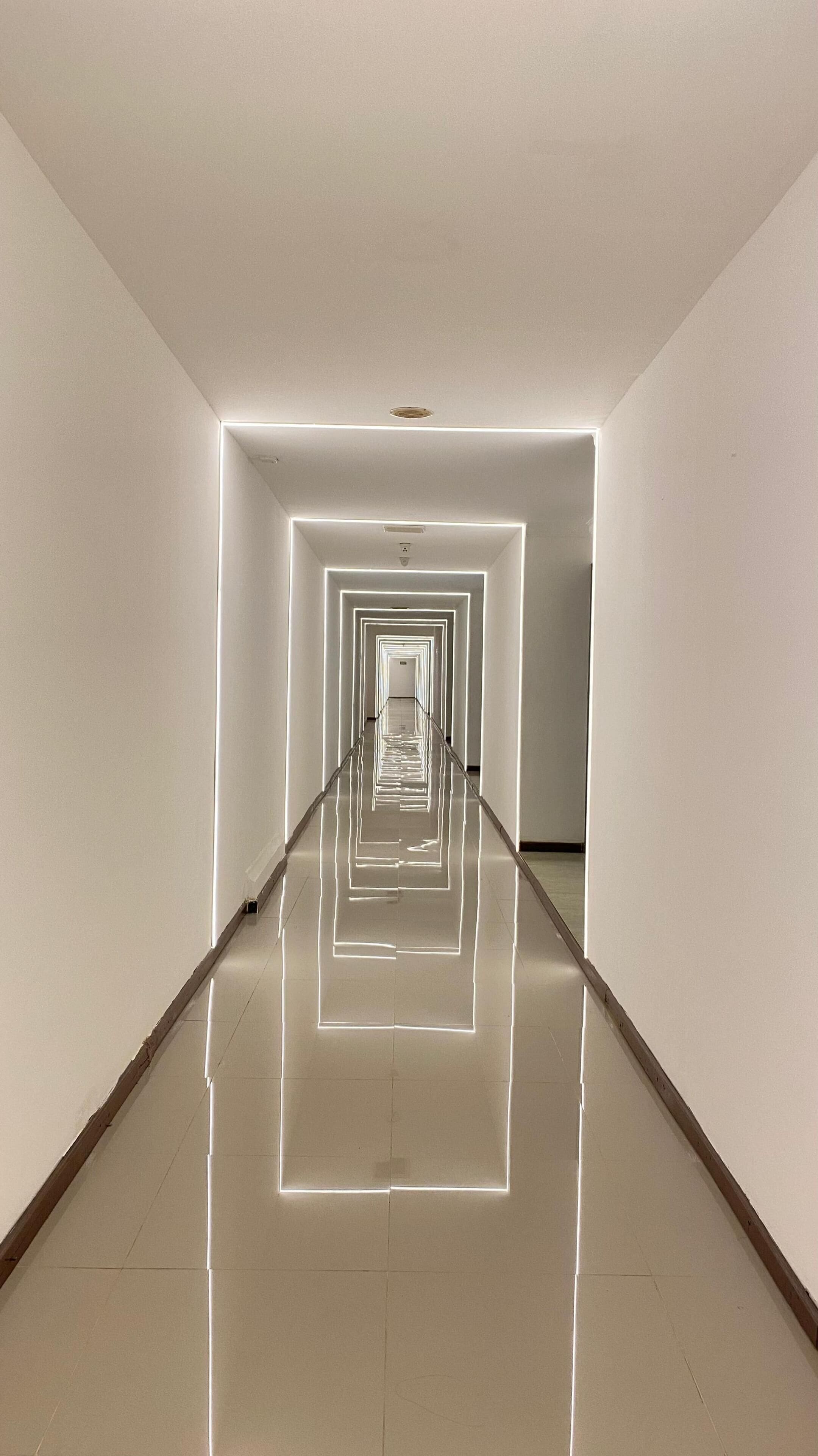 A corridor with reflective flooring and walls, leading to a door at the end.