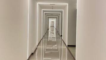 A corridor with reflective flooring and walls, leading to a door at the end.