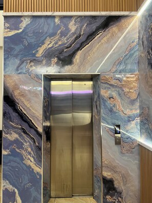 An elevator with a marble wall design. - Penuin Hotel (Batam)