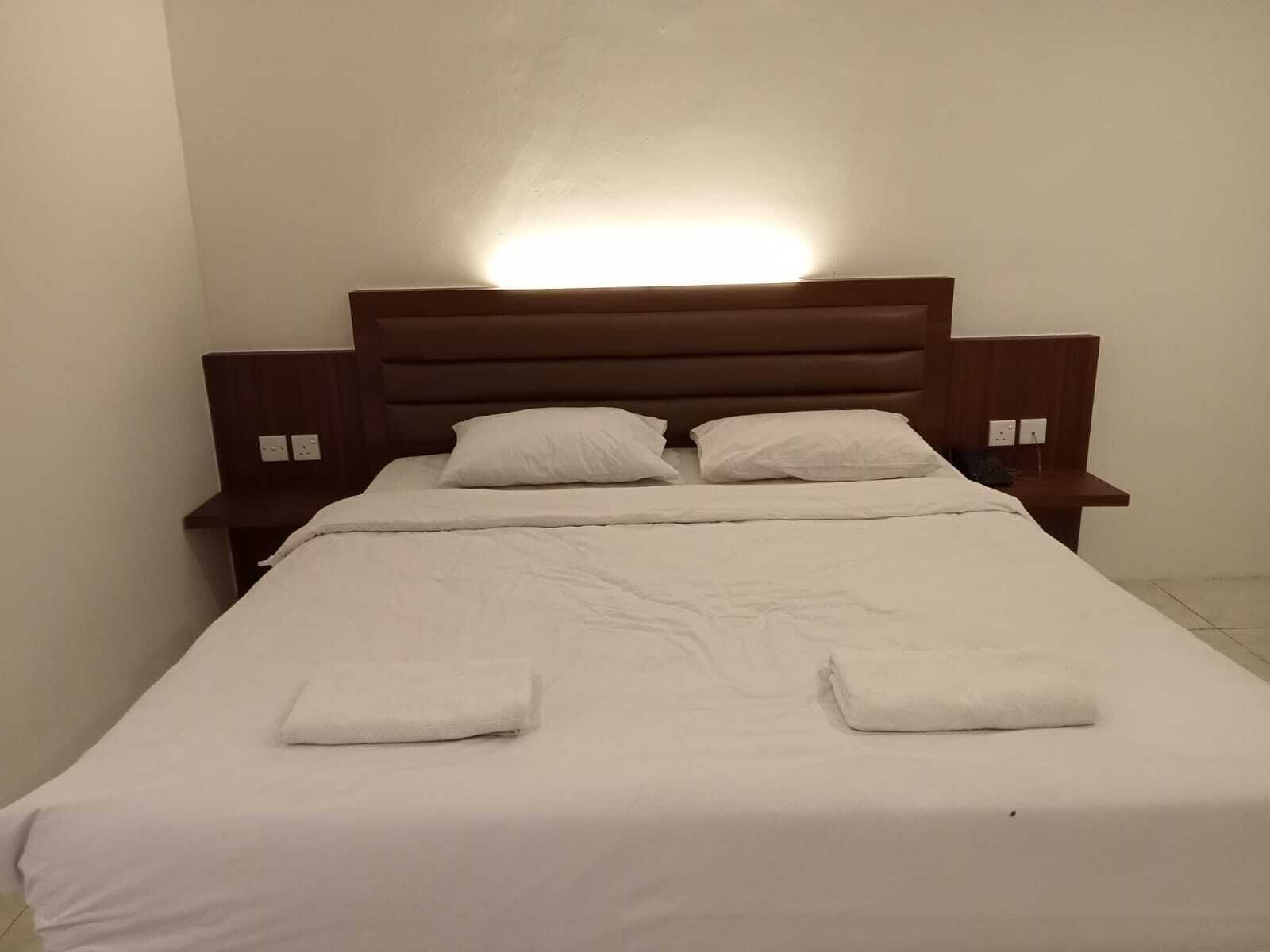 A neatly made bed with white linens and two pillows, a wooden headboard, and bedside tables with lamps.