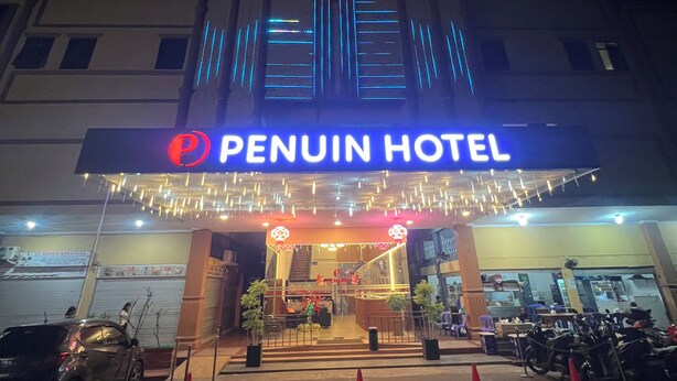 The exterior of the PENUIN HOTEL with a prominent illuminated sign, a gated entrance, and several motorcycles parked in front. - Penuin Hotel (Batam)