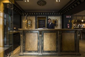A man reading at a marble reception desk with a glass enclosure and a bar area in the background. - La Calcina Suites (Venice)