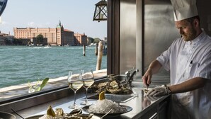 A chef preparing oysters with a view of a river and buildings in the background. - La Calcina Suites (Venice)